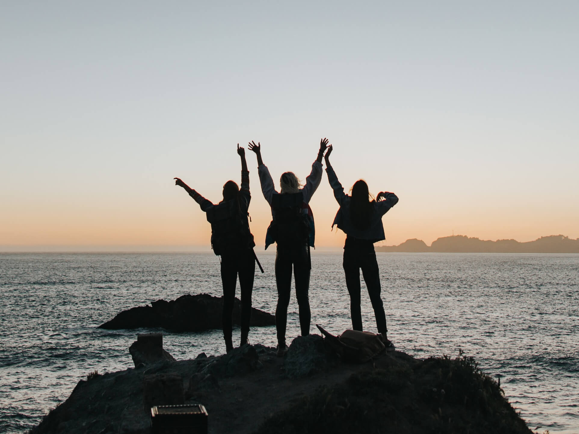 Silhouette photography of persons raising hands while standing on island